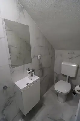 a white bathroom with a toilet and a mirror at Tadic apartments and rooms by the shore of Rama Lake in Prozor