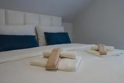 two towels on a white bed with blue pillows at Tadic apartments and rooms by the shore of Rama Lake in Prozor