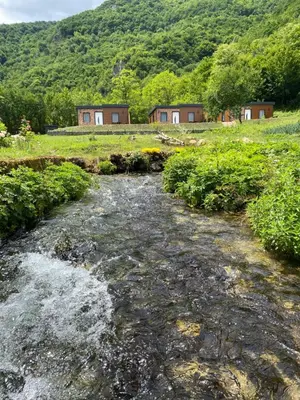 a stream in a field with houses in the background at Bungalovi izvor Plive 3 in Šipovo