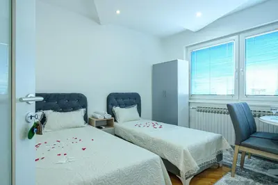 a room with two beds and a chair and windows at Evergreen Apartments in Visoko