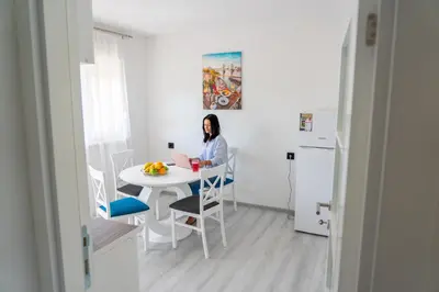 a woman sitting at a table in a kitchen with a laptop at Apartman Kruna in Drvar