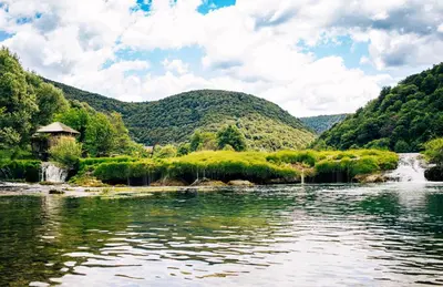 a river with a waterfall and mountains in the background at Natura na Uni in Bihać