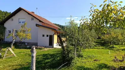 a small white house in a field with an apple tree at OZIM oaza zelenila i mira in Podrašnica
