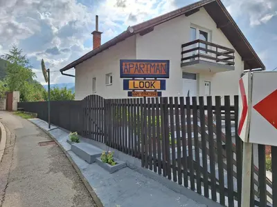 a white house with a fence and a sign at Apartman Look in Jajce