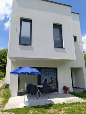 a house with a table and a blue umbrella at Apartman Una na dlanu, Novi Grad in Bosanski Novi