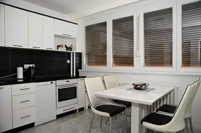 a kitchen with white cabinets and a white table and chairs at Apartman Lamela in Zenica