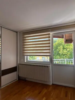 an empty living room with two windows with blinds at Apartman Siesta in Kiseljak