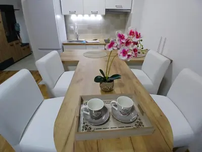 a dining room table with two cups and a vase with flowers at KEJ LUX Apartman in Bosanska Gradiška