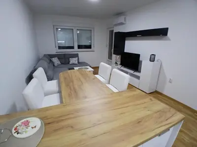 a living room with a wooden table and white chairs at KEJ LUX Apartman in Bosanska Gradiška