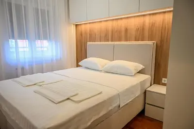 a bed with white sheets and white pillows and a window at Apartmani Galerija in Banja Luka
