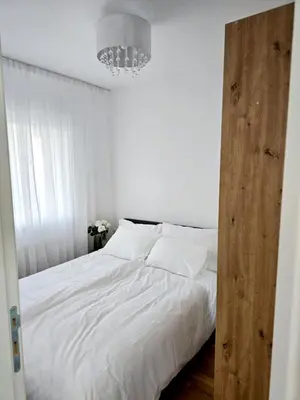 a bedroom with a bed with white sheets and a chandelier at A LUX APARTMAN Banja Luka in Banja Luka