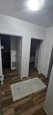an empty living room with a white rug on a wooden floor at Apartman Deny in Sanski most