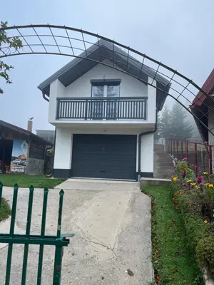 a white house with a garage and a fence at Vikendica Brljak in Gostilj