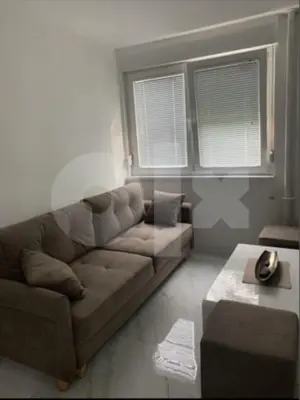 a living room with a brown couch and two windows at Apartman 078 in Banja Luka