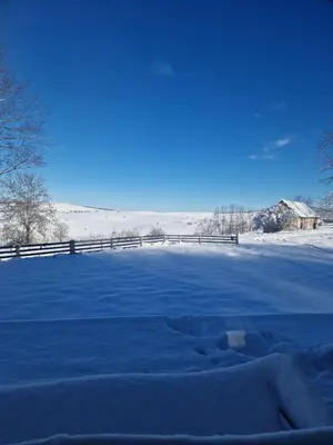 a snow covered field with a fence and a barn at Lukina koliba-vikendica-Manjaca in Banja Luka