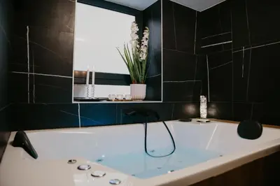 a bath tub in a bathroom with black tiles at Zapato Apartment Tuzla in Tuzla