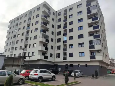 a large white building with cars parked in a parking lot at Apartman Luka in Doboj
