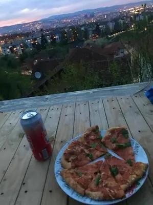 a plate of pizza on a wooden table with a drink at Studio apartman VB in Banja Luka
