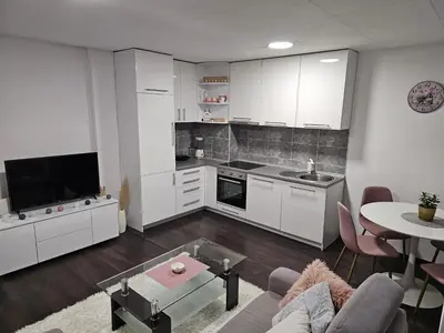 a kitchen with white cabinets and a living room at Apartman Nova Varos in Banja Luka