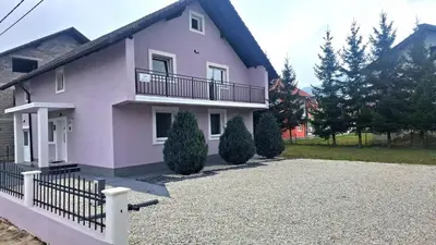 a pink house with a balcony and a driveway at Apartmani Biser Kupresa 4 in Kupres