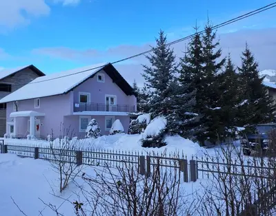 a white house with a fence in the snow at Apartmani Biser Kupresa 4 in Kupres