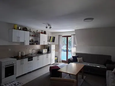 a kitchen and living room with white cabinets and a table at Apartman NANA Vlašić in Šišava