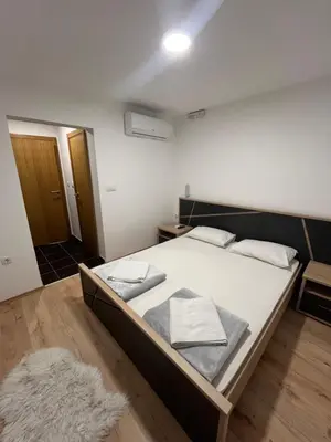 a bedroom with a bed with white sheets and a rug at Apartmani Karanovac in Banja Luka