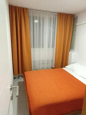 a bedroom with an orange bed and a window at Apartman Bulevar Živinice in Živinice