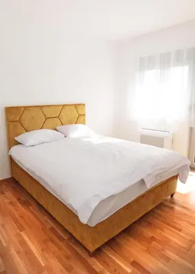 a bedroom with a bed with white sheets and a wooden floor at Apartman Dentalux 1 in Banja Luka