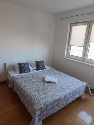 a bedroom with a bed with a blue blanket and two windows at Apartman AsHome in Banja Luka