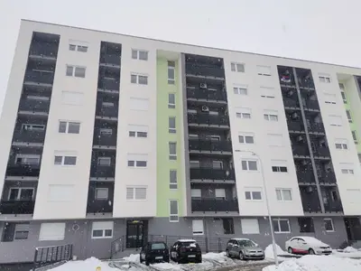 a large white building with cars parked in the snow at Apartman Stanko in Železnička Stanica Banja Luka Predgrađe