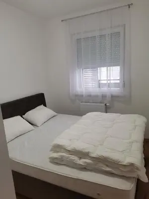 a bed with white sheets in a room with a window at Apartman Stanko in Železnička Stanica Banja Luka Predgrađe