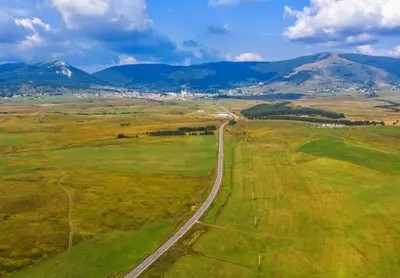 a road in a field with mountains in the background at Kupres Apartman555 in Kupres