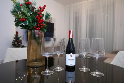 a bottle of wine and four wine glasses on a table at Apartment Feel Banja Luka in Banja Luka