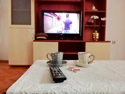 a remote control and two cups on a table with a television at Apartman Doboj in Doboj