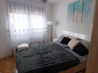 a bedroom with a bed with a gray blanket and a window at Stan na dan Relax in Bosanska Dubica