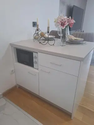 a white cabinet with a microwave and a vase of flowers at Apartman NINA in Doboj