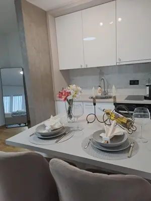 a kitchen with white cabinets and a table with plates at Apartman NINA in Doboj
