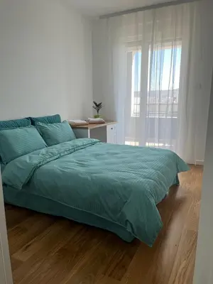 a white bedroom with a bed with a green comforter at Apartman Delta in Banja Luka