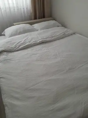 an unmade bed with white sheets and pillows at City Center Moku Apartman in Zenica