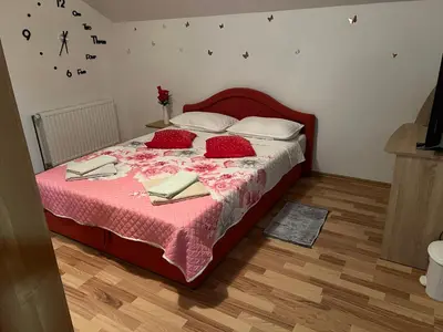 a bedroom with a bed with red sheets and a clock on the wall at Halal Holidey Kuća za odmor in Spahići