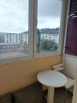 a table and a chair in a room with two windows at City apartmant in Tuzla