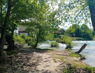 a riverbank with trees and benches next to a river at Apartman Orhideja in Bihać