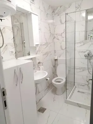 a white bathroom with a toilet and a glass shower at Boulevard Tuzla Studio Apartment in Tuzla