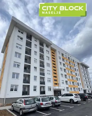 a large white building with cars parked in a parking lot at Apartman ADA in Železnička Stanica Incel