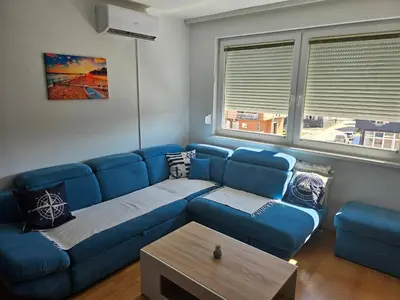 a living room with a blue couch and two windows at Apartman Dona in Bosanska Gradiška