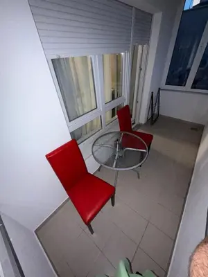 a balcony with a glass table and two red chairs at San apartment in Banja Luka