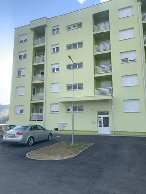 a yellow building with a car parked in a parking lot at Stan na dan Gradiška in Bosanska Gradiška