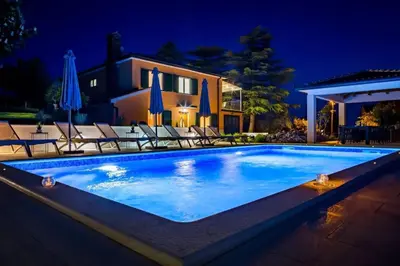 a swimming pool in front of a house at night at Villa Imperio Deluxe in Brekovica
