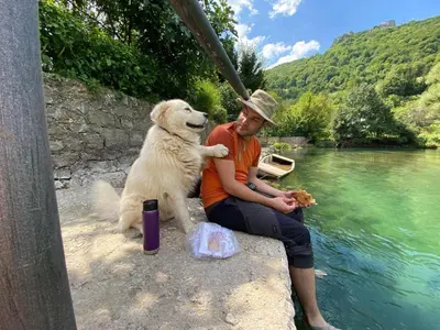 a man and a dog sitting next to a body of water at Domaćinstvo Una-Ostrovica in Kulen Vakuf